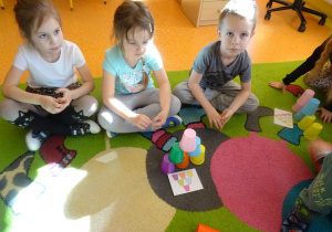 Dzieci siedzą przed ułożoną wieżą z kubeczków według wzoru na kartce.